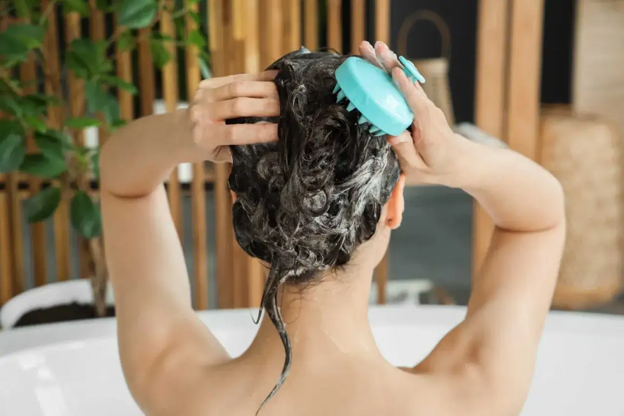 Une personne se lave les cheveux avec un accessoire bleu, profitant de ce moment pour se laver les cheveux une fois par semaine.