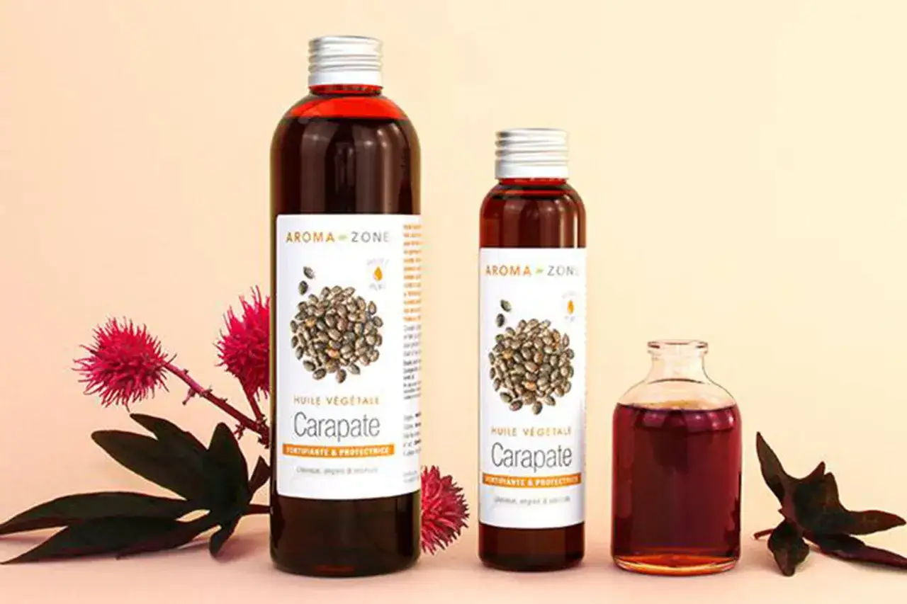 Trois bouteilles d'huile de carapate, aux multiples bienfaits, sont présentées avec des fleurs et feuilles.