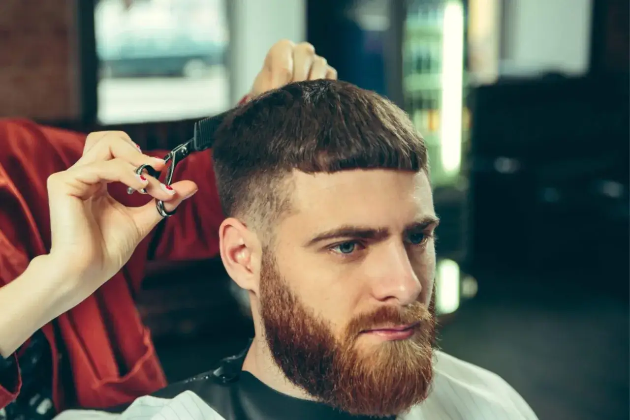 Un homme à la barbe rousse se fait couper les cheveux, un style coupe coiffé décoiffé homme tendance.