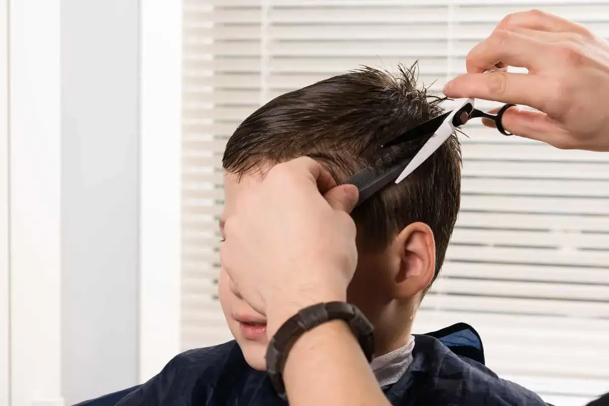 Un coiffeur utilise un peigne et des ciseaux pour un couper cheveux enfant.