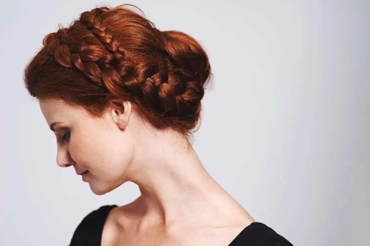 Une femme aux cheveux roux mi-longs arbore un chignon tressé élégant, encadrant son visage tourné de profil.