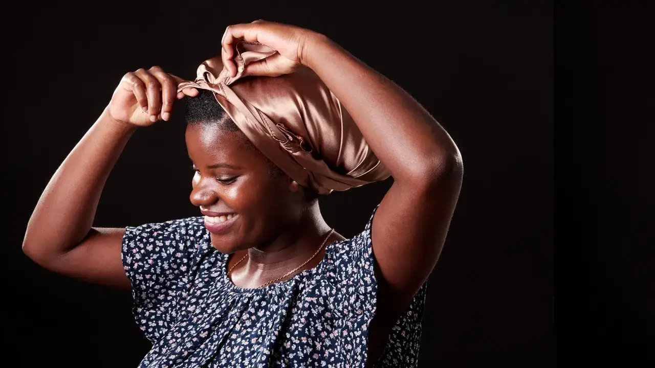 Une femme ajuste son foulard en satin, une coiffure protectrice nuit idéale pour préserver ses cheveux.