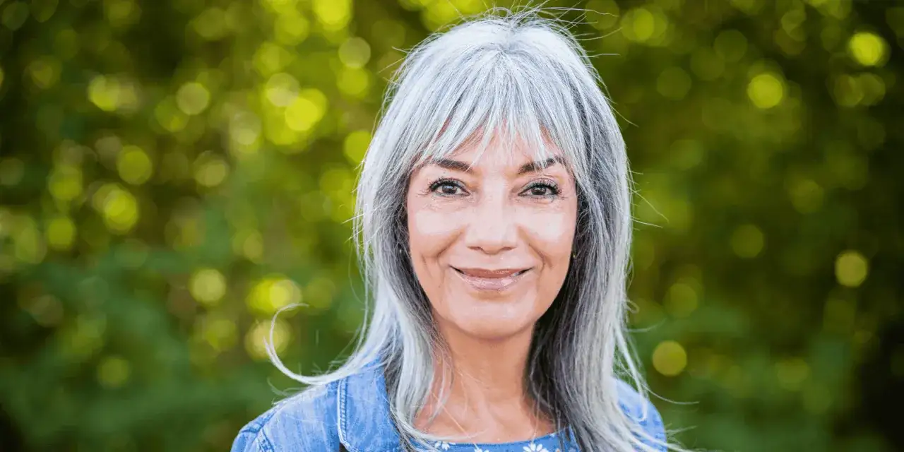 Une femme blonde aux cheveux argentés souriante, une inspiration pour comment cacher ses cheveux blancs avec élégance.