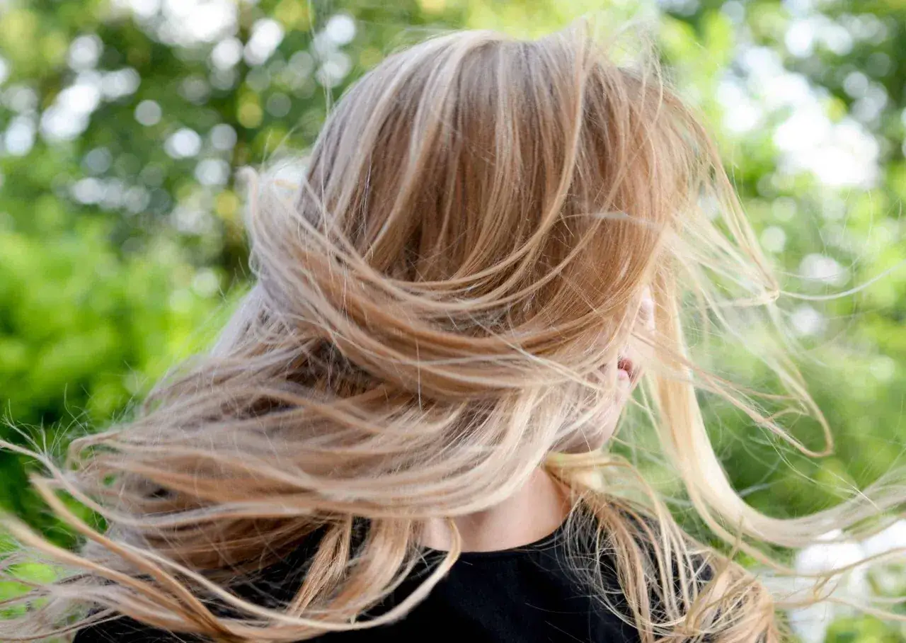 Chevelure blonde balay&eacute;e par le vent, &eacute;voquant l'id&eacute;e de faire un balayage maison pour un look naturel et lumineux.