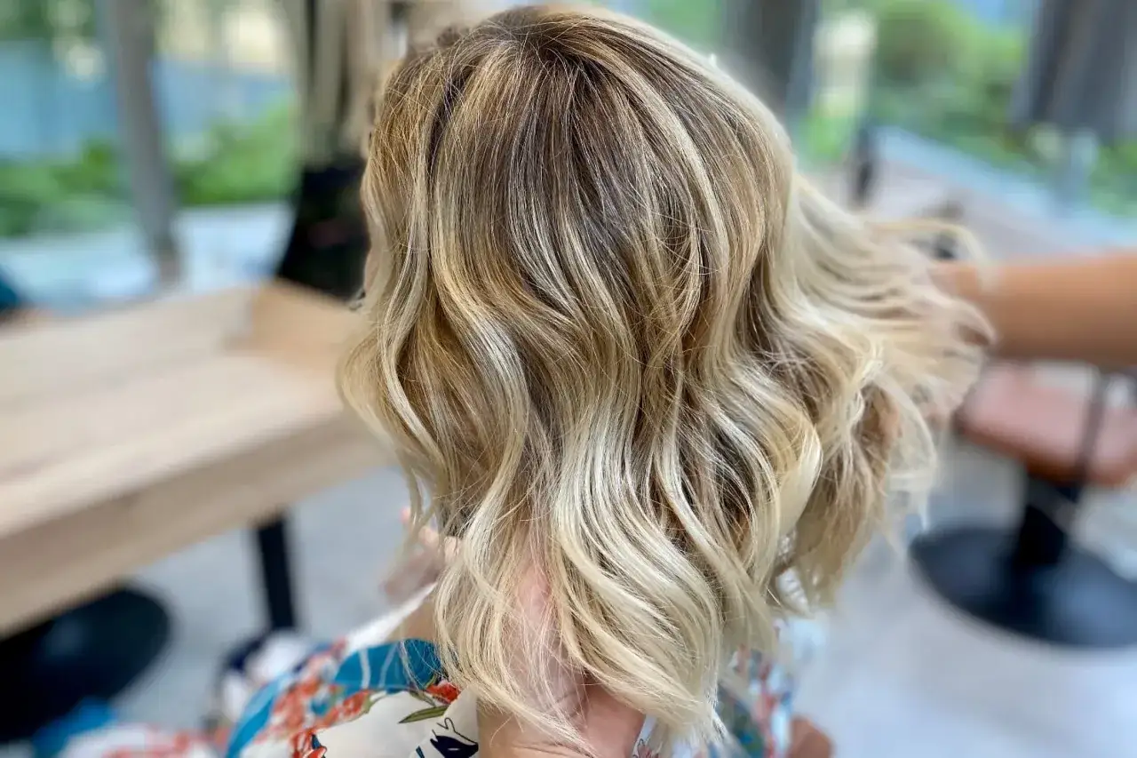 Chevelure blonde aux reflets subtils, un dégradé naturel en ton sur ton qui capte la lumière.