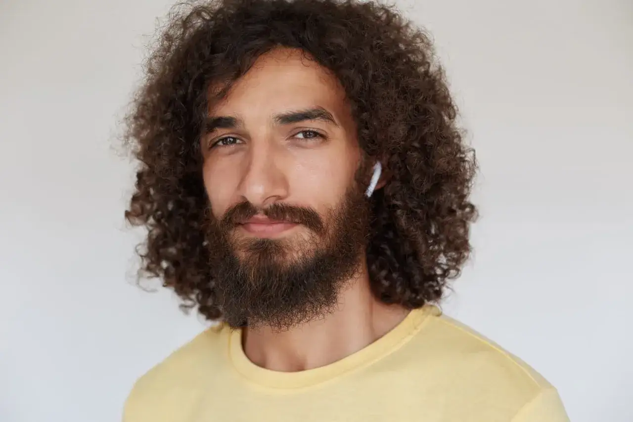 Un homme avec une magnifique coiffure cheveux frisés, une barbe et un écouteur blanc.
