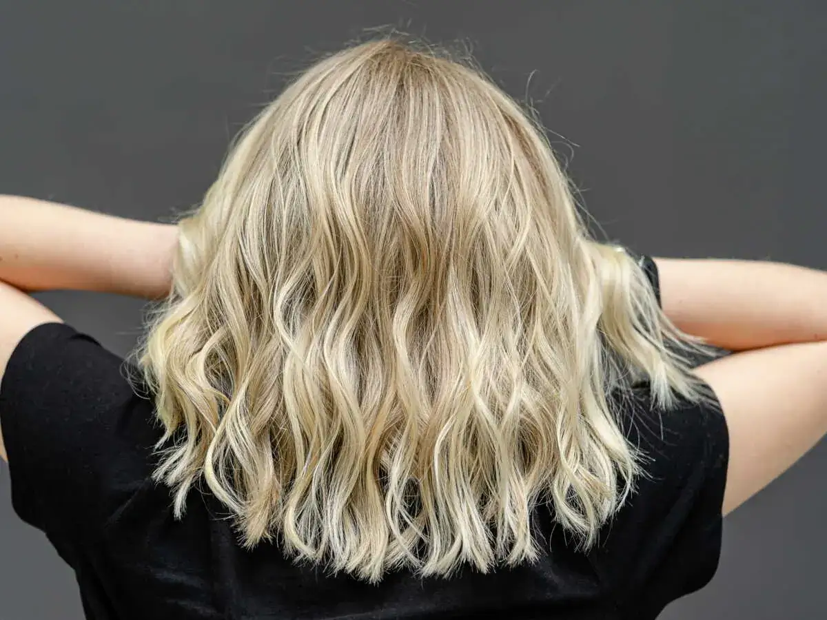 Vue arrière d'une femme aux cheveux blonds, mi-longs et ondulés, formant un joli carré ondulé.