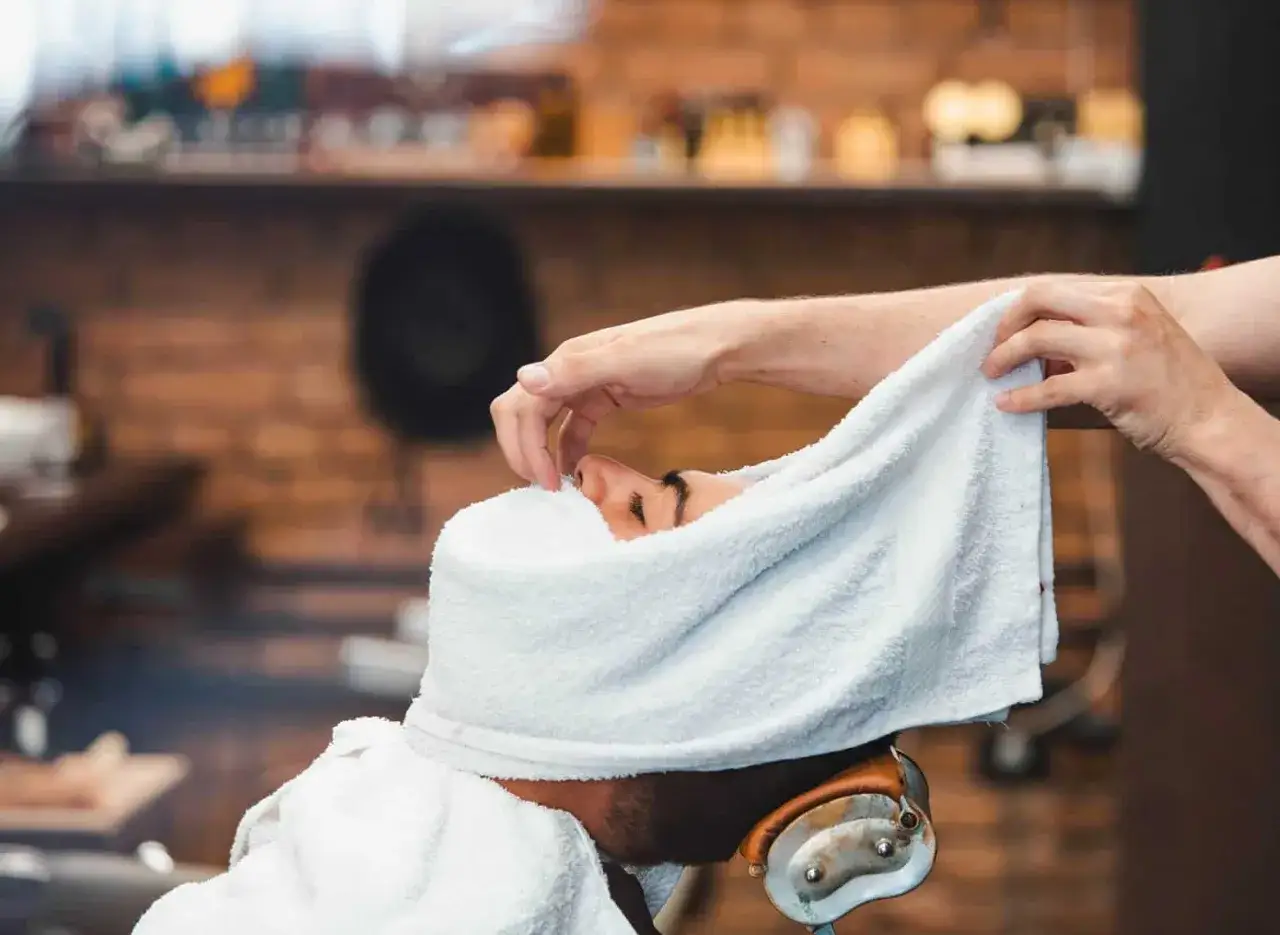Un homme re&ccedil;oit un soin du visage avec une serviette chaude. Apprenez comment faire une serviette chaude pour les cheveux pour un moment de d&eacute;tente.