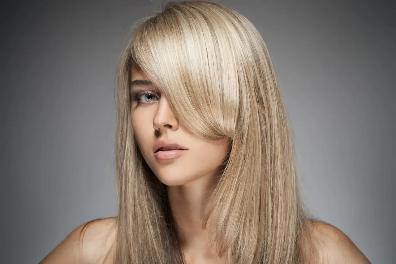 Une femme aux cheveux blonds avec un balayage subtil, une frange effilée encadrant son visage.