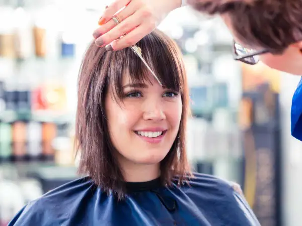 Une coiffeuse ajuste la frange d'une cliente souriante, finalisant une coupe carré.