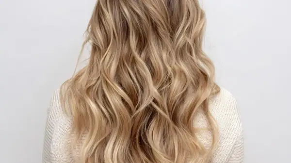 Chevelure ondulée aux reflets blonds subtils, un effet babylight blond naturel et lumineux.