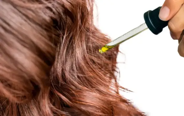 Une goutte d'huile tombe sur des cheveux bruns. Un geste simple pour mettre de l'huile sur les cheveux tous les jours pour les nourrir.