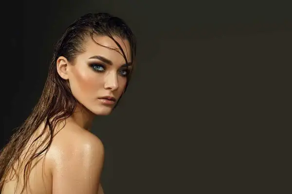 Jeune femme au regard intense, cheveux mouillés et peau luisante, un look aquatique saisissant.