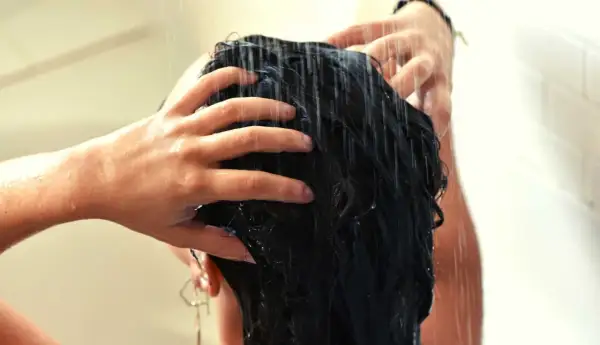 Mains massant des cheveux mouillés sous la douche, comme un soin au beurre de karité cheveux sans rinçage pour une douceur intense.