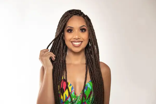 Une femme souriante aux box braids, portant un maillot de bain coloré, joue avec ses tresses.