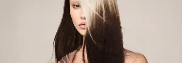 Une femme au regard intense, ses longs cheveux bruns contrastent avec des mèches blondes lumineuses. Un balayage inversé avant après spectaculaire.