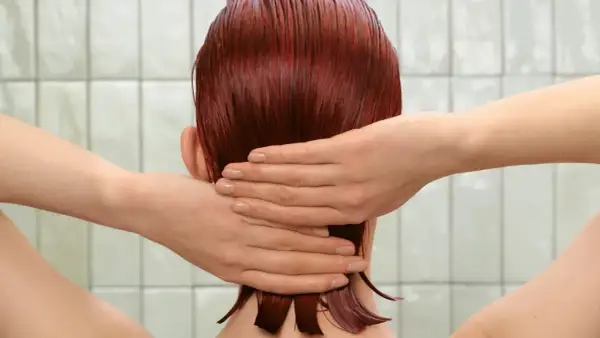 Mains massant des cheveux roux mouillés, peut-être après l'application d'un shampoing violet pour raviver la couleur.