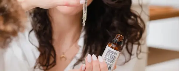 Une femme montre comment appliquer un sérum avec une pipette, une goutte dorée tombant sur sa main.
