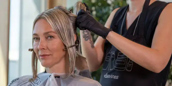 Une coiffeuse applique une couleur ou une mèche pour cacher les cheveux blancs d'une cliente.