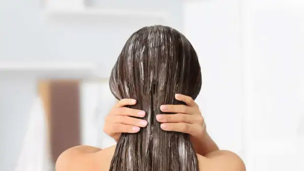 Application d'un soin pour une clarification cheveux. Les mains appliquent le produit sur les longueurs.