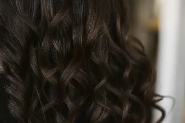 Chevelure brune aux reflets chauds, la couleur gloss cheveux révèle des ondulations soyeuses et lumineuses.