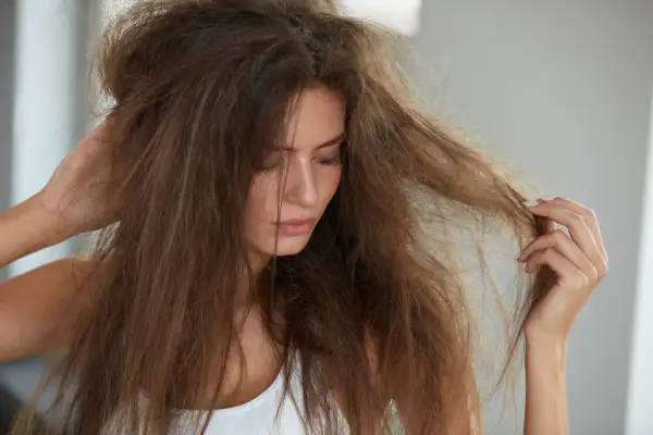 Femme touchant ses cheveux emmêlés, visiblement secs et abîmés, souffrant de cheveux cassants et fourchus.