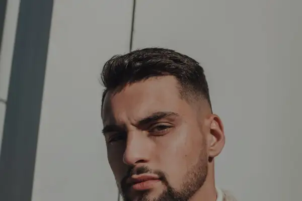 Un homme au chignon homme rasé, regard intense, sous un soleil éclatant.