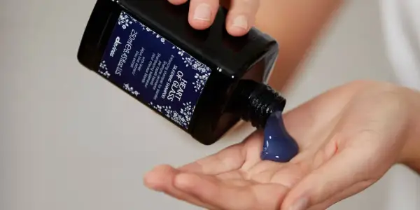 Une main verse un shampoing bleu, idéal pour les cheveux blonds, dans une autre main.