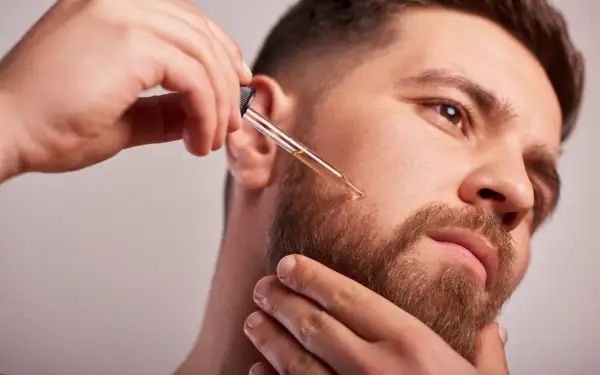 Un homme applique de l'huile de ricin sur sa barbe avec un compte-gouttes pour une pousse plus dense et soyeuse.