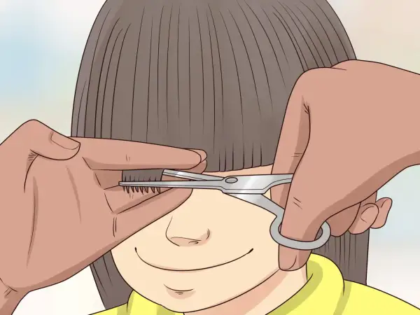 Une main tient une mèche de cheveux d'un enfant pour un couper cheveux enfant. Des ciseaux s'approchent pour la coupe.