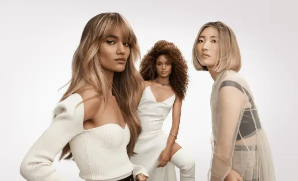 Trois femmes aux coiffures sublimes. La première arbore un french balayage blond, la deuxième des boucles rousses, la troisième un carré blond platine.