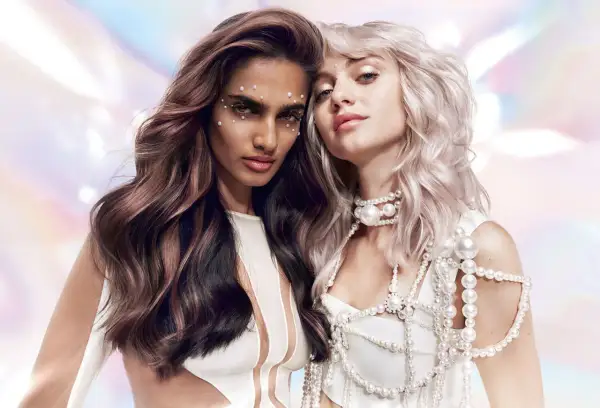 Deux femmes aux cheveux longs et ondulés, l'une brune avec des reflets roses, l'autre blonde platine. Leurs visages sont ornés de perles. Le **dialight sur cheveux sec ou humide** sublime leurs mèches.