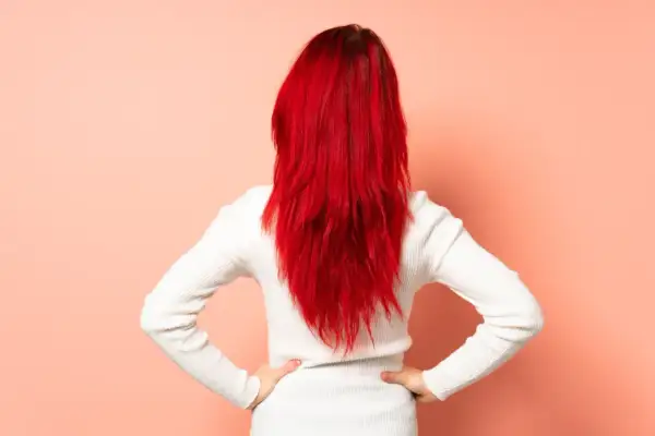 Vue arrière d'une femme aux cheveux rouge vif, cherchant comment enlever une coloration rouge naturellement.