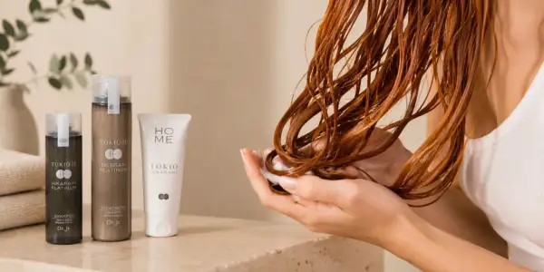 Mains douces appliquant un soin sur des cheveux bouclés roux, avec des produits Tokio Inkarami. Idéal pour la décoloration cheveux bouclés.