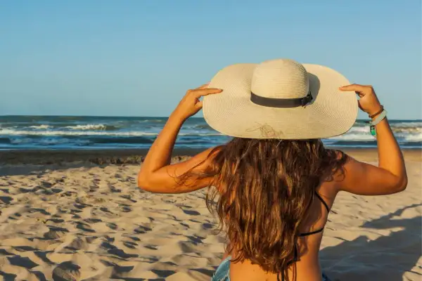 Une femme à la plage, coiffée d'un grand chapeau, montre comment protéger ses cheveux du soleil.