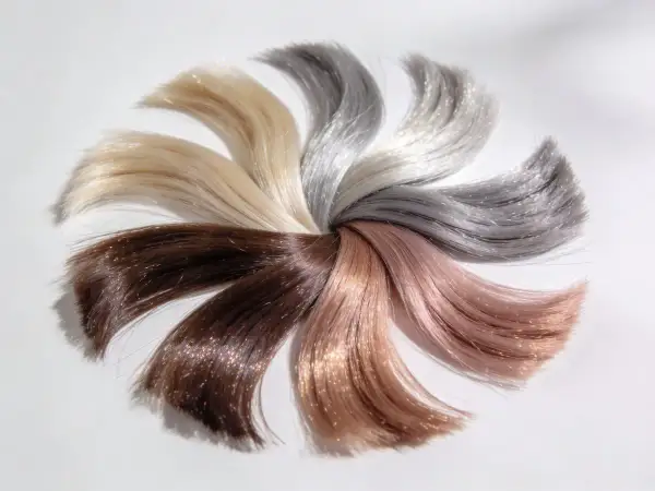 Échantillons de cheveux aux teintes variées, du brun au blond platine, disposés en éventail. Un fond d'éclaircissement subtil met en valeur les reflets chatoyants.