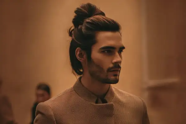 Un homme au chignon homme stylé, portant une veste texturée, regarde au loin.