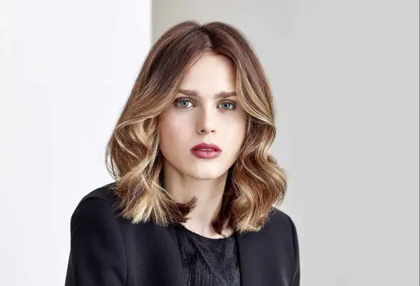 Une femme au regard intense, ses cheveux mi-longs aux reflets blonds et châtains, un parfait exemple de *ombre hair contouring*.