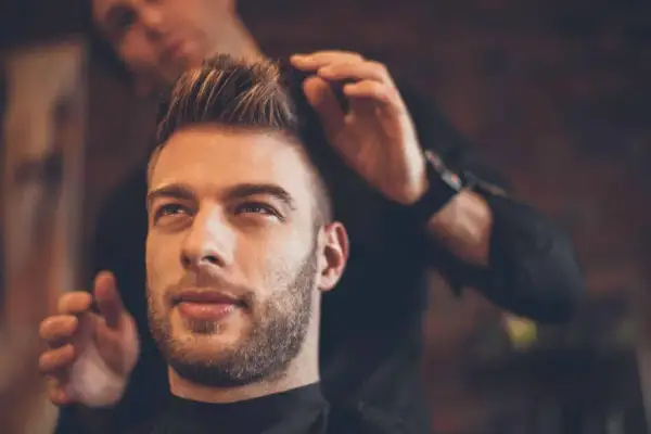 Un homme au regard pensif se fait coiffer une coupe pompadour par un barbier.