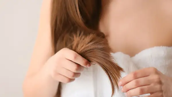 Une femme examine ses cheveux, cherchant des conseils pour comment éviter les fourches et garder une chevelure saine.