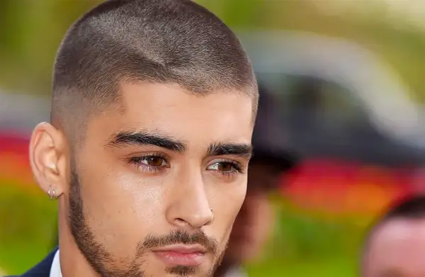 Un jeune homme au regard intense arbore une coupe buzz, ses cheveux courts et nets accentuent son style moderne.