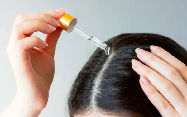 Une main applique une goutte d'huile de chanvre sur le cuir chevelu, une solution naturelle pour les cheveux blancs.