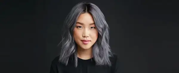Une jeune femme au teint clair arbore une chevelure mi-longue, ondulée et d'un magnifique gris argenté. Elle porte un haut noir.