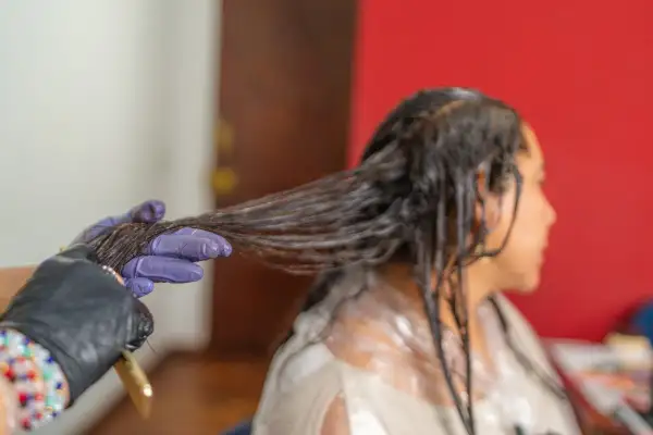 Application d'une patine sur cheveux humides. Une main gantée sépare une mèche pour une application uniforme.