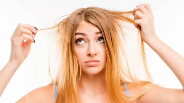 Une jeune femme aux cheveux jaune regarde ses mèches emmêlées avec une expression perplexe.