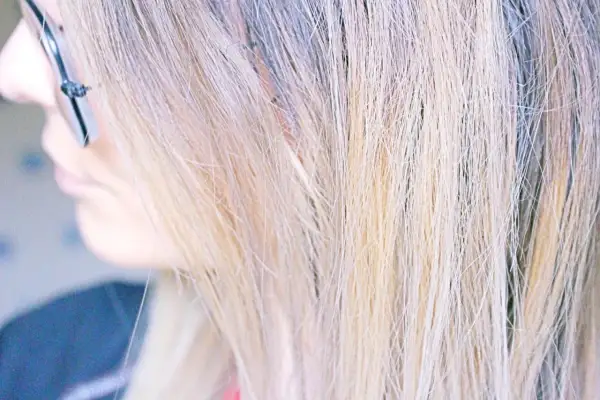 Une femme se regarde dans le miroir, son regard concentré sur l'idée d'enlever une patine cheveux. Ses mèches blondes sont mises en valeur.