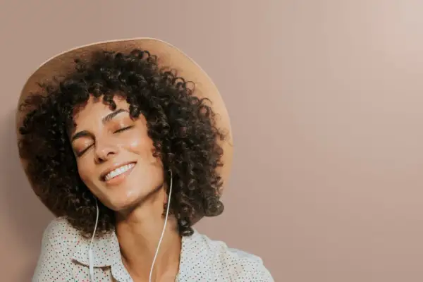 Femme avec une permanente naturelle, un chapeau et des écouteurs, profitant d'un moment de détente.