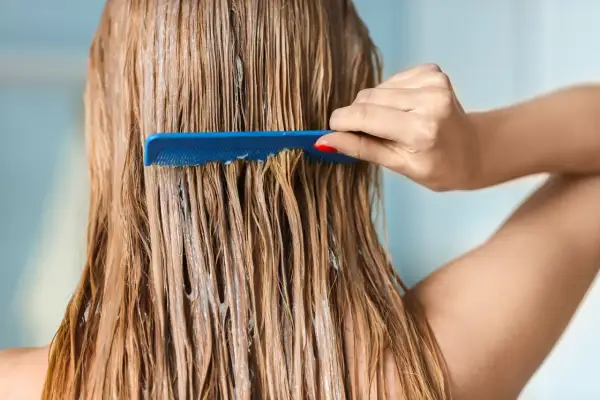 Une main peigne des cheveux blonds mouillés, recouverts d'un soin, peut-être pour changer de couleur de cheveux.