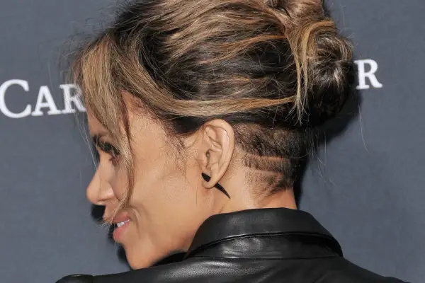 Une femme aux cheveux longs arbore un undercut audacieux avec des motifs rasés sur le côté.
